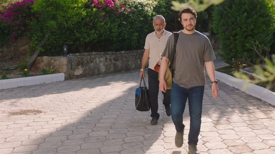Still from About My Mom: a father and son walking with their bags