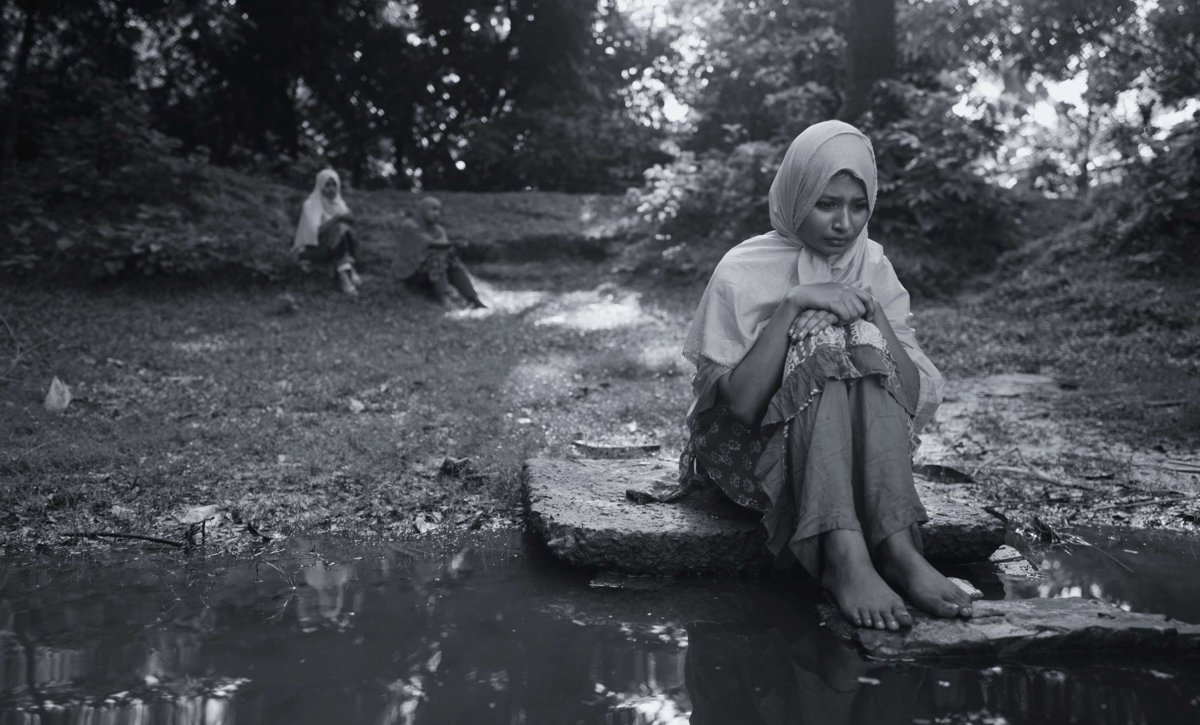 Black-and-white still from The Blind Girl and an Elephant: a young woman in a headscarf sitting on a stone by a pool of water