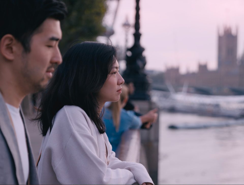 Still from The Distance We Drift: a man and a woman by the Thames, Westminster behind them