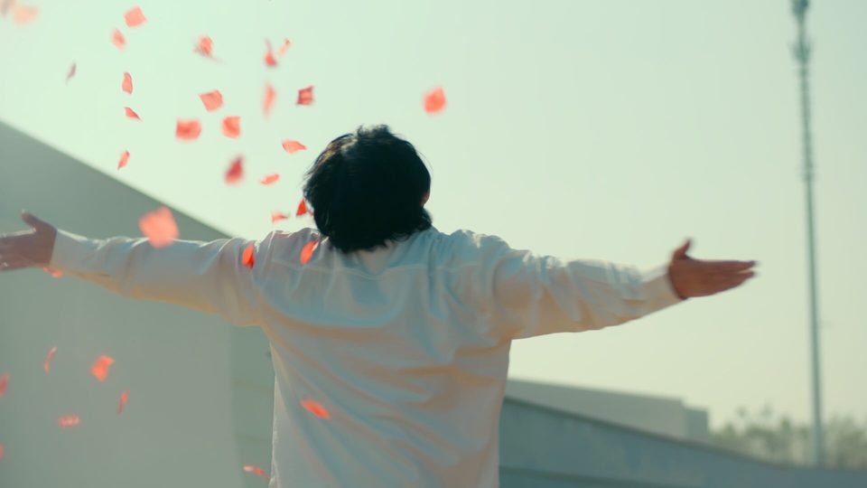 Still from From Falling Petals to New Bloom: a man with arms outstretched as petals fall around him