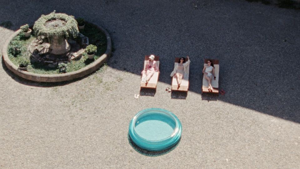 Still from Glorious Summer: three girls sunbathing beside a fountain and a paddling pool, seen from above