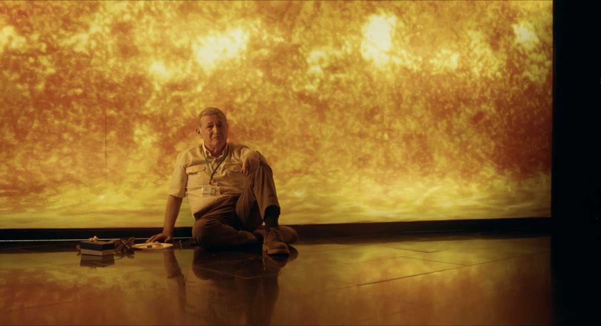 Still from Those Who Whistle After Dark: an older man sitting on the floor in front of a glowing orange screen